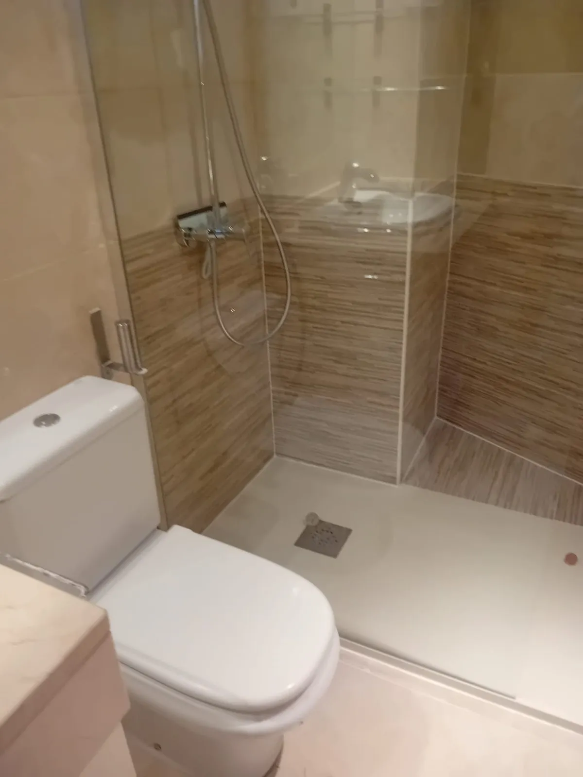 Baño reformado con plato de ducha, mampara de cristal y alicatado imitación madera