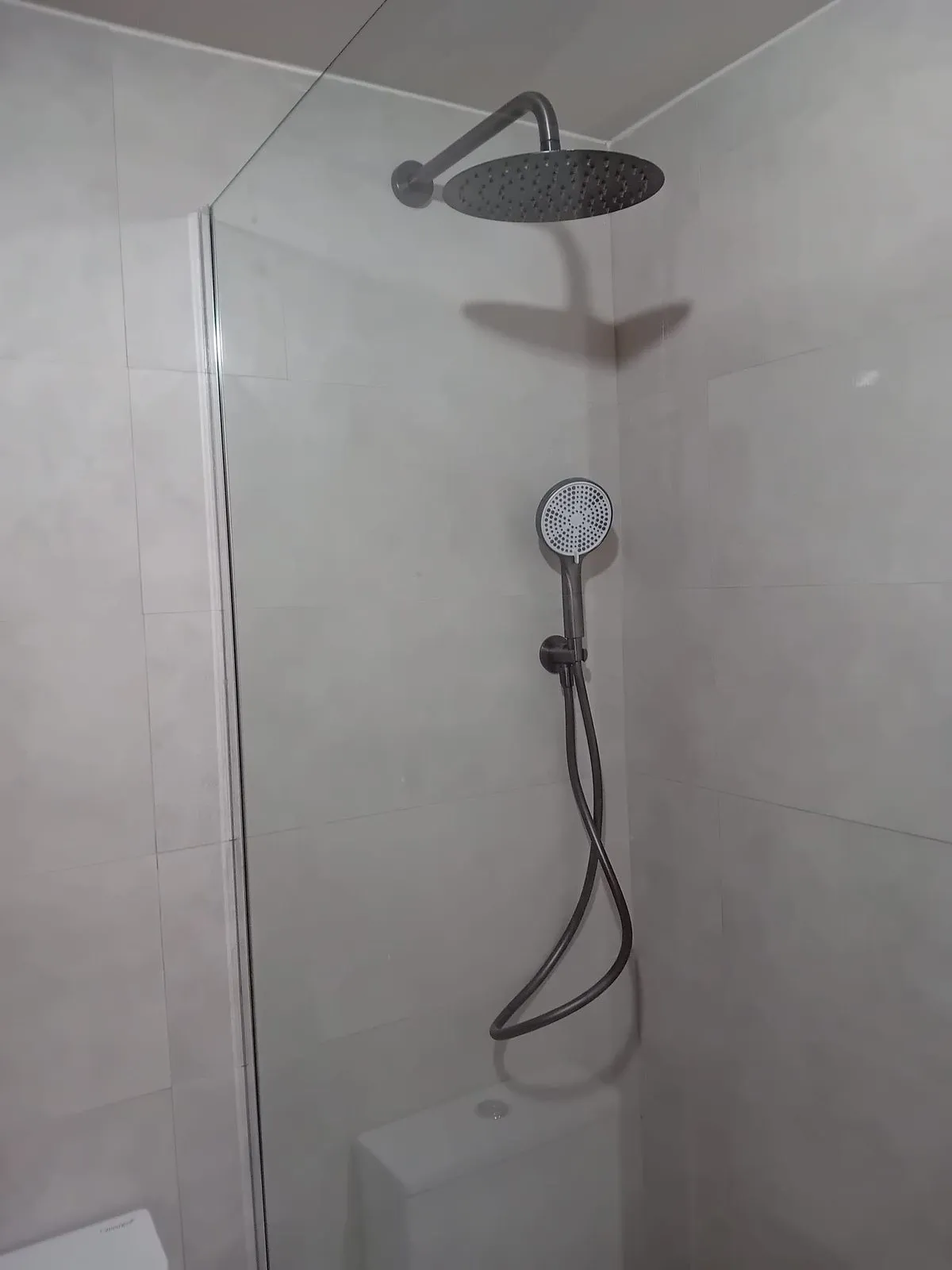Rociador de lluvia y teléfono de ducha en negro sobre porcelánico gris claro